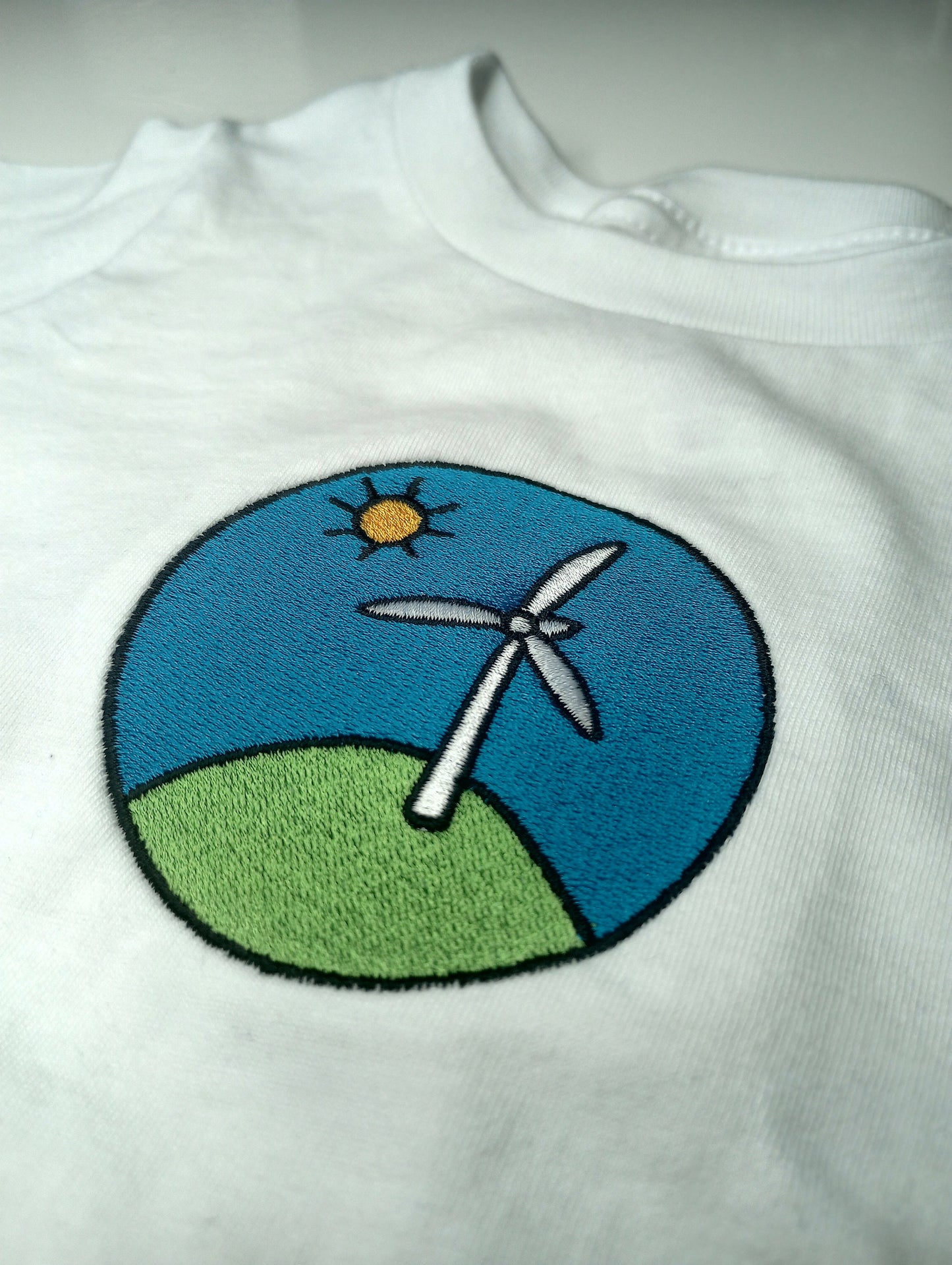 White shirt with embroidered design of a wind turbine on a blue background

